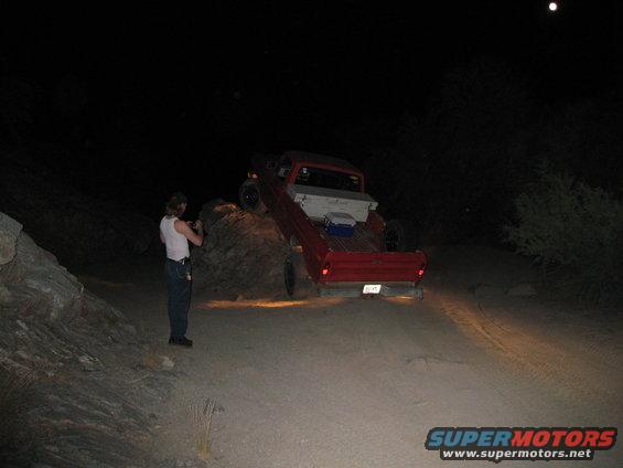 Red pickup truck with a white toolbox in the bed, angled on a dirt incline at night