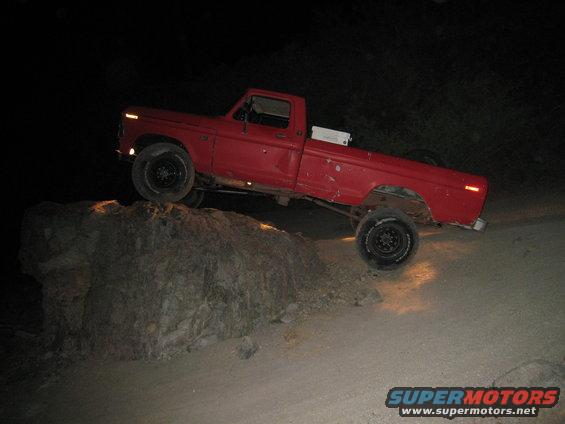 Red pickup truck with lifted suspension navigating a large rock off-road
