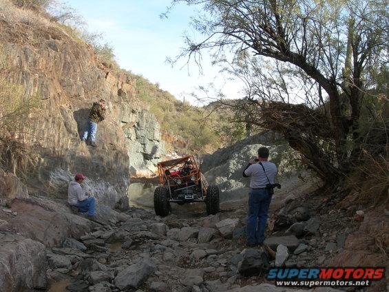 Off-road buggy navigating a rocky canyon with two people watching