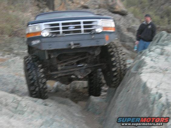 Dark blue Ford F-250 off-roading on rocks, front view. Modified bumper and large tires