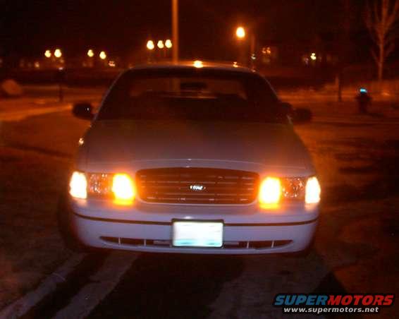 Front view of a 1998 Ford Crown Victoria with illuminated headlights and amber turn signals