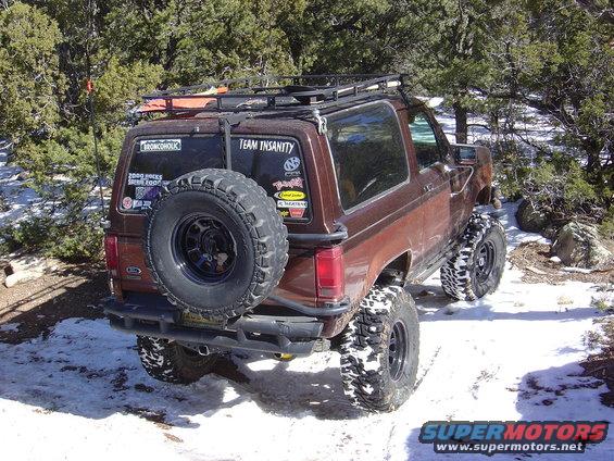 Brown 1986 Ford Bronco II with a roof rack and spare tire on the back, parked in a snowy, wooded area