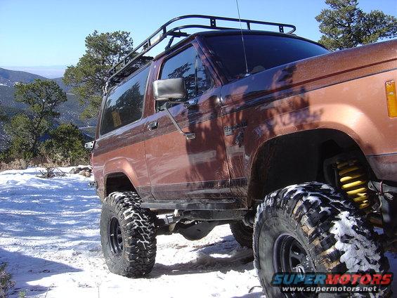 Brown Ford Bronco II with roof rack and large tires in snow