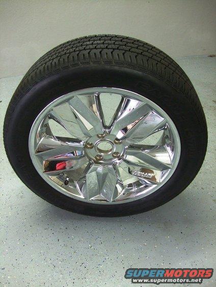 Chrome wheel with a tire on it, sitting on a speckled floor