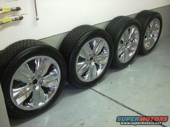 Four chrome wheels with tires lined up against a wall