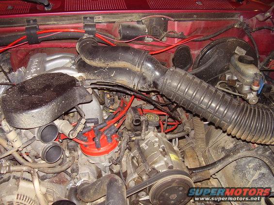 Engine bay with red distributor cap, air intake hose, and AC compressor