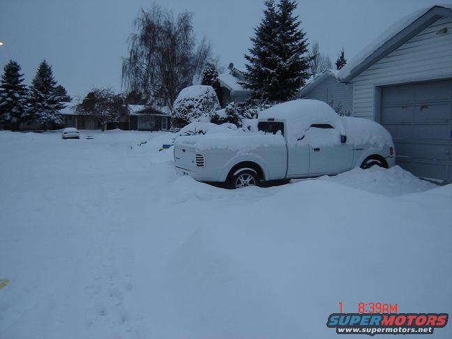 White pickup truck buried in snow next to a garage
