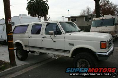 White extended cab pickup truck with a camper shell, parked next to a trailer and a motorhome