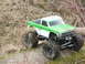 1996 Ford Bronco - RC monster truck with large tires on a dirt path, partially obscured by branches.