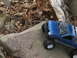 1996 Ford Bronco - A blue pickup truck toy is positioned on a large rock amidst fallen leaves and branches.
