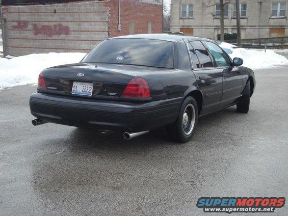 Black 2000 Ford Crown Victoria sedan, rear view, with dual exhaust pipes and a license plate reading AA 2222