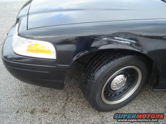 Front fender and wheel of a dark 2000 Ford Crown Victoria with damage on the fender