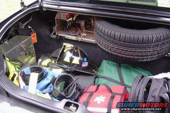 Car trunk packed with firefighter helmet, radio, medical bags, and spare tire