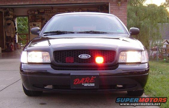 Front view of a black 2003 Ford Crown Victoria police car with a DARE license plate and a red light on the grille