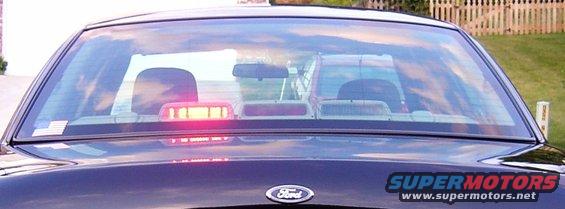 Rear view of a Ford Crown Victoria with a light bar inside and another vehicle reflected in the rear window