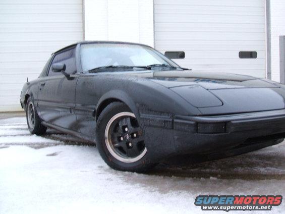 Black 1983 Mazda RX-7 parked in front of a garage door with snow on the ground
