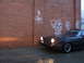 1983 Mazda RX-7 - A dark coupe with pop-up headlights is parked next to a graffiti-covered brick wall.