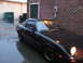 1983 Mazda RX-7 - Dark coupe with pop-up headlight parked next to a brick wall on a wet day.