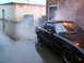 1983 Mazda RX-7 - Steam billows from the engine compartment of a black Mazda RX-7 in a wet alleyway.