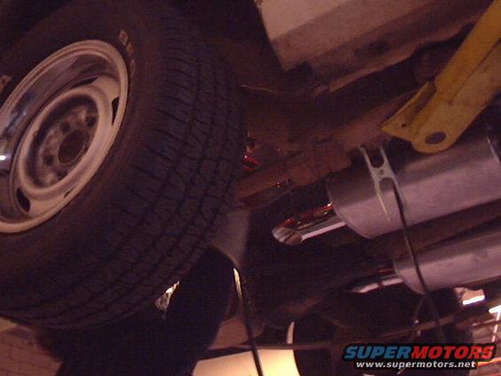 Underside view of a car's wheel and exhaust pipes. SuperMotors logo visible