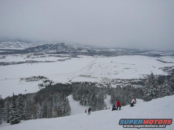 Snowy mountain landscape with skiers on a slope and a distant town