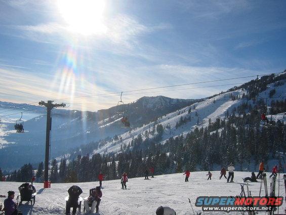 Skiers on a slope with chairlifts going up the mountain under a bright sun