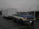 1990 Ford Bronco - A blue and white pickup truck tows a white trailer on a cloudy day.