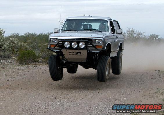 Silver Ford Bronco mid-air jump on a dirt road, desert landscape