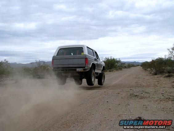 Bronco airborne on dirt road, kicking up dust. White top, grey body