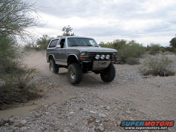 1980 Ford Bronco driving on a dirt road, kicking up dust