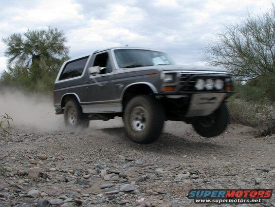 Gray Ford Bronco kicking up dust on a rocky trail, front bumper modified with lights