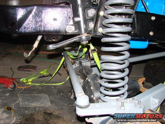 Close-up of vehicle front suspension with large coil spring, tie rod, and straps