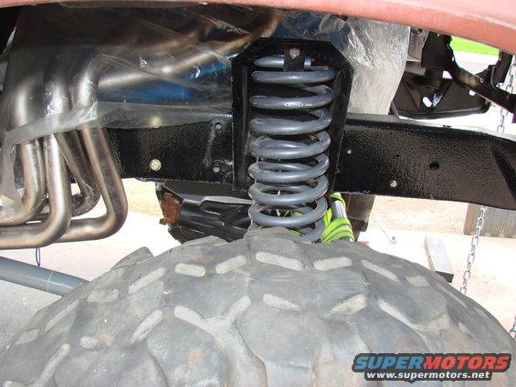 Close-up of a vehicle's front suspension coil spring and exhaust headers