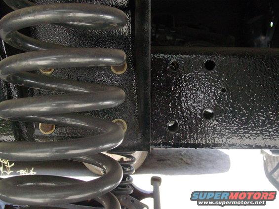 Close-up of a large coil spring and black painted frame section of a vehicle