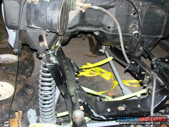 Close-up of a vehicle's frame, suspension, and engine bay area with yellow straps holding parts