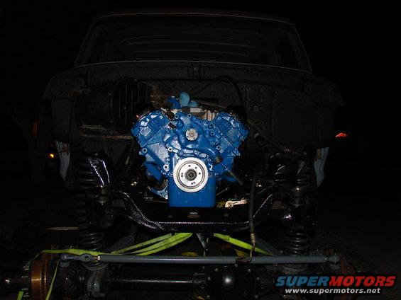 blue engine in a vehicle frame, front end removed, suspension visible