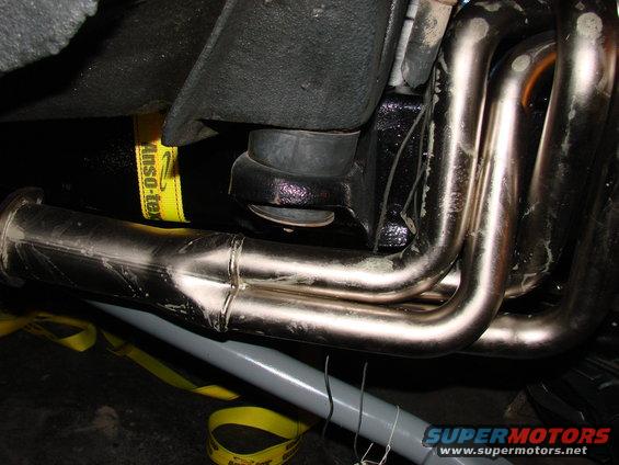 Close-up of exhaust headers and yellow tie-down straps attached to suspension components