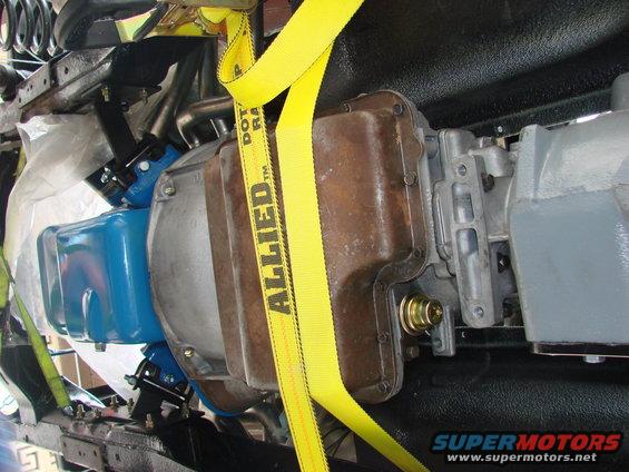 Close-up of vehicle's transmission and transfer case assembly, held by yellow straps. Some parts are blue, others are brown and gray