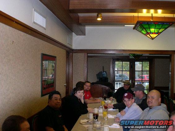 Restaurant interior with people at a table and a reflection of a vehicle in a framed picture