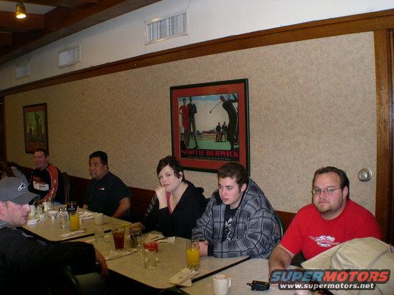 People seated at tables in a restaurant, with a golf-themed picture on the wall