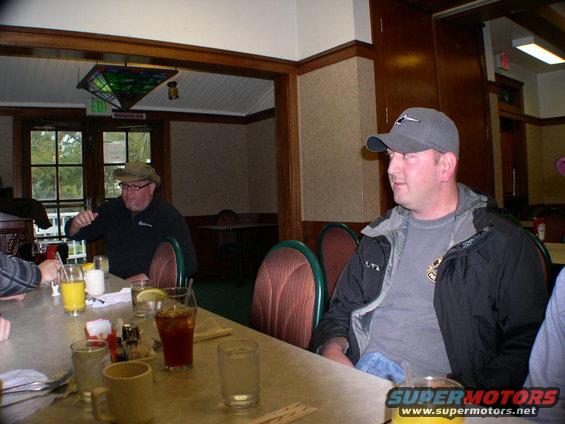 Two men sit at a table in a restaurant with drinks and condiments