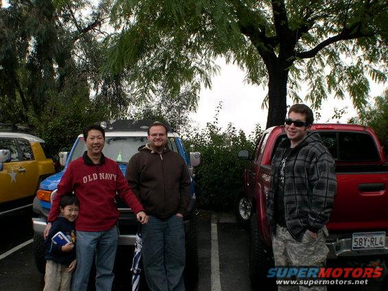 Two Toyota FJ Cruisers and a red pickup truck parked outside with three people standing in front of them