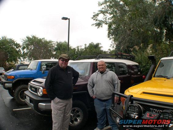 Three Toyota FJ Cruisers in blue, maroon, and yellow parked in a lot with two men standing in front