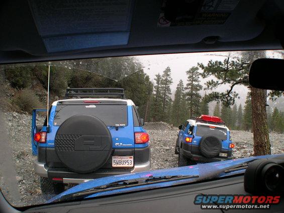 Two blue 2007 Toyota FJ Cruisers on a gravel road, rear view