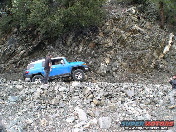 Blue 2007 Toyota FJ Cruiser navigating a rocky trail with a person standing beside it