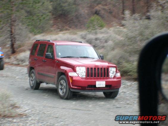 Red Jeep Liberty on a gravel road, front 3/4 view. License plate reads ARD763