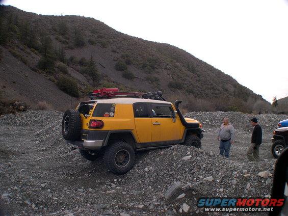 Yellow 2007 Toyota FJ Cruiser on a rocky trail with two people standing nearby