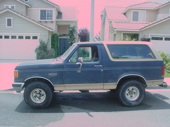 1986 Ford Bronco parked on street, side view. Blue body with tan trim