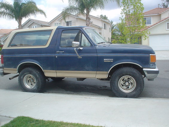 Blue Ford Bronco parked on street, tan trim, aftermarket wheels