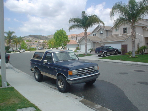 Blue 1987 Ford Bronco parked on a suburban street, tan trim, slightly dirty